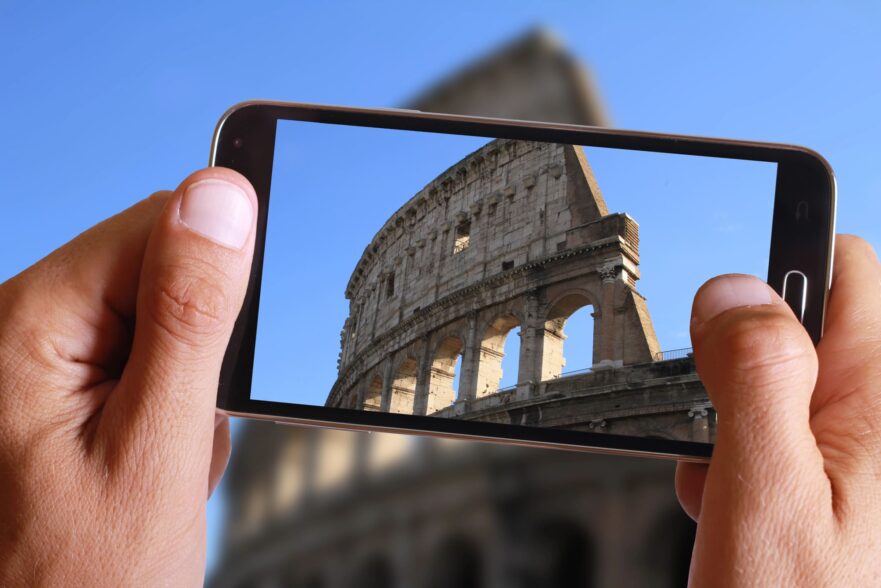 Mano maschile che scatta foto al colosseo di Roma con cellulare. Vacanza italiana - Depositphotos_85035880