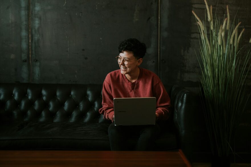 Uomo sorridente che usa il computer portatile mentre è seduto sul divano in pelle nera - Brooke Cagle (Unsplash)